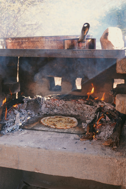 French onion soup pizza baking on a Baking Steel set on an open wood fire, surrounded by coals and flame