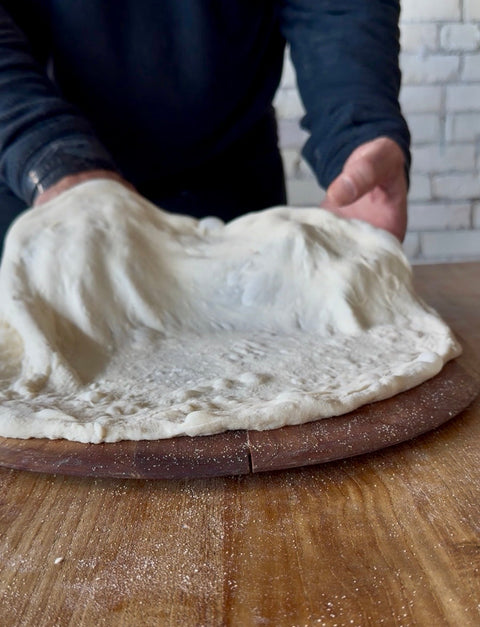 24 hour pizza dough stretched out and being placed on the pizza peel