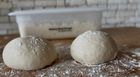 two 72 hour pizza dough balls on the counter with a batch of dough in a container in the background