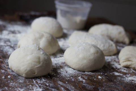 72-hour cold fermented pizza dough balls on a floured wooden surface, ready for baking.