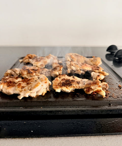 Seared chicken thighs with golden brown crust cooking on a Baking Steel Mini Griddle on an electric stovetop, smoke rising