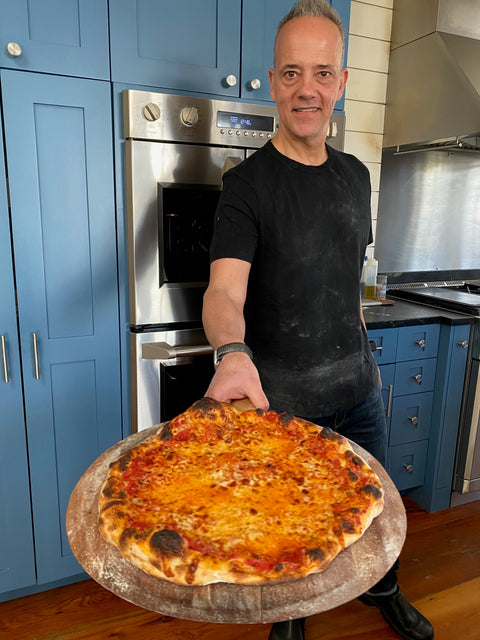 Andris Lagsdin, inventor of the Baking Steel, holding a freshly baked pizza in his home kitchen