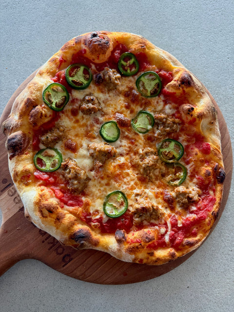 Sausage and jalapeño pizza on a Baking Steel wooden peel with blistered crust