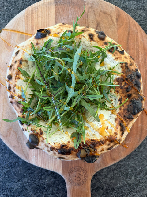Ricotta pizza with arugula and hot honey on a cherry wood peel