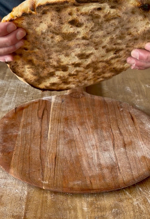 Hands lifting a pizza to show the leopard-spotted charred undercarriage baked on a Baking Steel