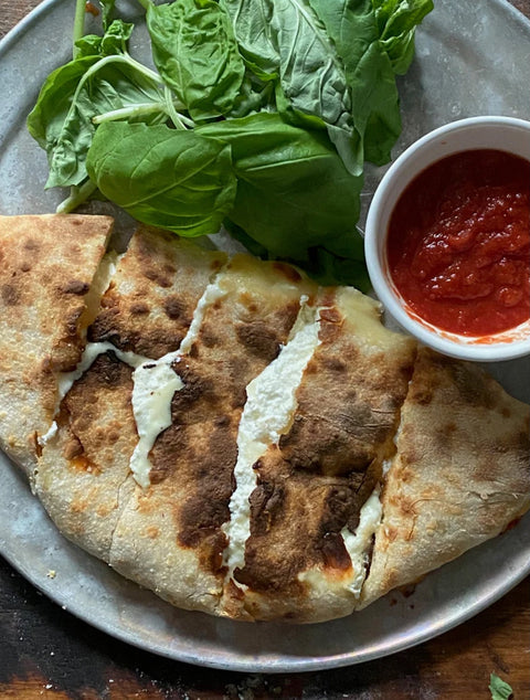 cheese calzone plated with fresh basil and ramekin of tomato sauce