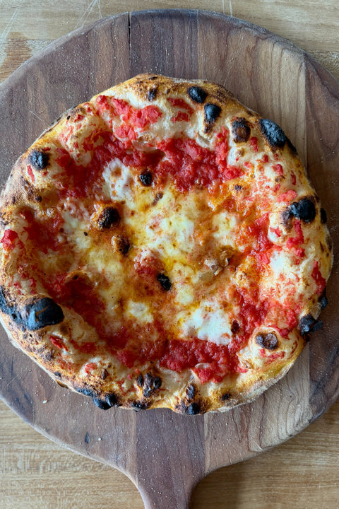 A rustic homemade pizza on a wooden peel, topped with a two-cheese base of fresh mozzarella and fontina over red tomato sauce, with creamy white cheese pools and a blistered, leopard-spotted crust baked on a Baking Steel.