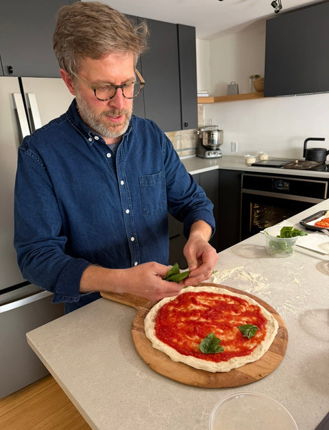 Chef Paul Berglund layering fresh basil onto a pizza before the bake