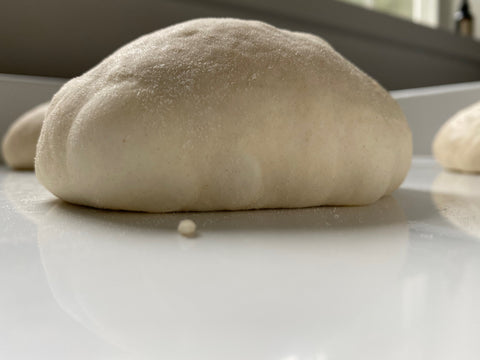 Perfectly proofed pizza dough ball dusted with flour on a kitchen counter, ready to stretch and bake