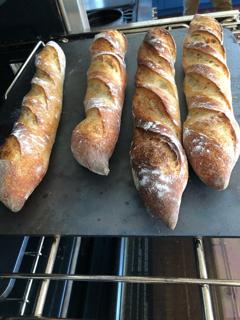 Four crusty homemade baguettes with golden brown crust and open scoring fresh out of the oven on a Baking Steel