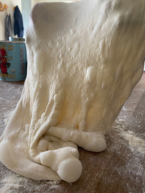 72-hour fermented pizza dough stretching on a floured wooden board