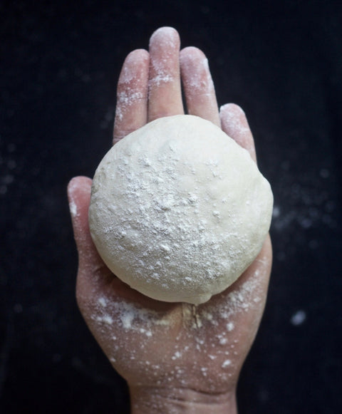 Close-up of a smooth pizza dough ball resting in a floured hand