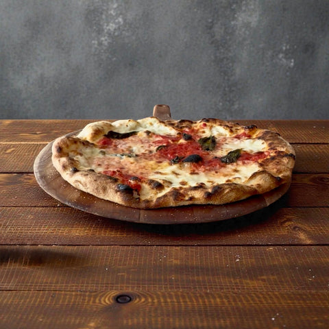 a new jersey style margherita fresh out of the oven on a pizza peel on a wood table.