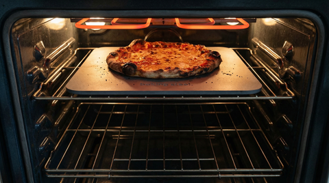 Pizza baking inside an oven on a Baking Steel with visible heating elements.